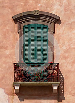 Italian balcony with iron railing, red flowers and closed shutters to keep the sun out