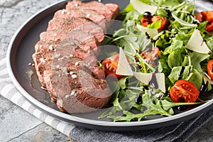 Italian Beef Tagliata salad with wild rocket, cherry tomatoes and parmesan cheese close-up on a plate. Horizontal