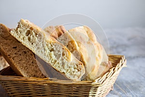 Italian bread of Focaccia Genovese type on display on a basket on a wooden table, sliced in squared pieces.
