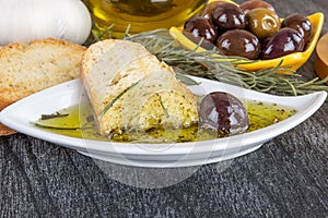 Italian Bread with Oil for Dipping with Herbs & Spices. Olive oil sauce in white bowl & Greek olives on wood background