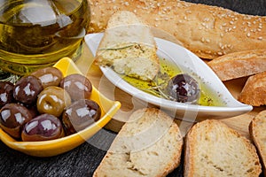 Italian Bread with Oil for Dipping with Herbs & Spices. Olive oil sauce in white bowl & Greek olives on wood background