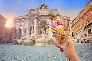 Italian bright sweet ice cream gelato cone with different flavors held in hand on the background of famous Trevi Fountain