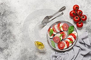 Italian Caprese salad with chopped tomatoes, mozzarella, basil, olive oil on a light stone background. Top view, flat lay, copy