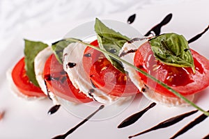 Italian Caprese salad. Mozzarella cheese, tomatoes and basil herb leaves. Balsamic vinegar arranged on white plate