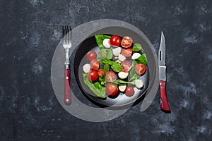 Fresh italian caprese salad with mozzarella and tomatoes on black plate over dark stone background with copy space, flat