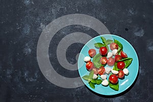 Fresh italian caprese salad with mozzarella and tomatoes on blue plate over dark stone background with copy space, flat