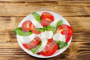 Italian caprese salad with tomatoes, mozzarella cheese and basil on wooden table. Top view