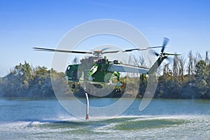 Italian CFS 103 fire fighting helicopter flying over a lake to collects water through a suction tube to extinguish a fire