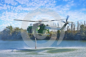 Italian CFS 103 fire fighting helicopter flying over a lake to collects water through a suction tube to extinguish a fire