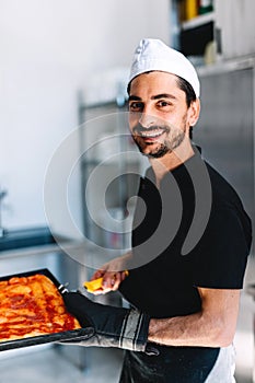 Italian chef pizzaiolo putting pizza to oven in restaurant kitchen