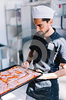 Italian chef pizzaiolo putting pizza to oven in restaurant kitchen