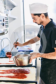Italian chef pizzaiolo putting tomato sauce on pizza in restaurant
