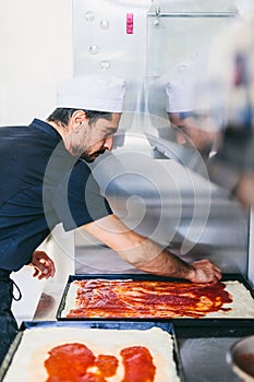 Italian chef pizzaiolo putting tomato sauce on pizza in restaurant