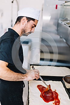 Italian chef pizzaiolo putting tomato sauce on pizza in restaurant