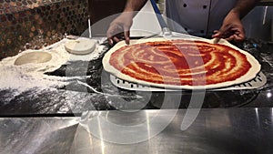 Italian chef prepares pizza dough with sauce at a restaurant