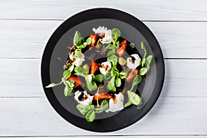 Italian cuisine. Fresh italian caprese salad with mozzarella and tomatoes on dark plate on white wooden table. Top view.