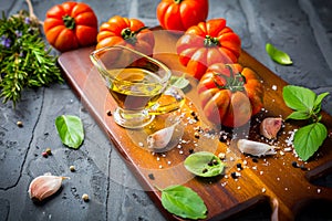 Italian cuisine - Olive oil, tomato and herbs on rustic cutting board