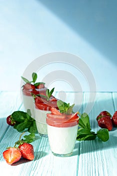 Italian dessert Panakota with strawberry coolies, fresh berries and mint on a blue background with hard shadows. Creamy milk