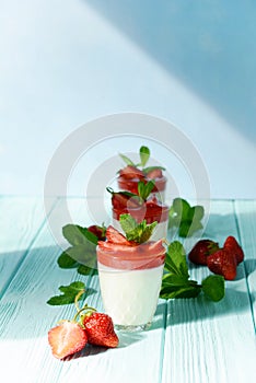 Italian dessert Panakota with strawberry coolies, fresh berries and mint on a blue background with hard shadows. Creamy milk