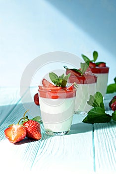 Italian dessert Panakota with strawberry coolies, fresh berries and mint on a blue background with hard shadows. Creamy milk