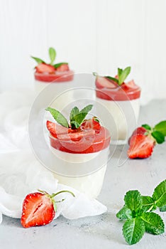 Italian dessert Panakota with strawberry coolies, fresh berries and mint on a white background with hard shadows.