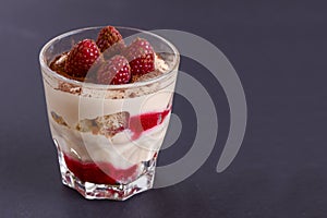 Italian dessert panna cotta with raspberries and cocoa powder served in small glass over black background.