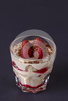 Italian dessert panna cotta with raspberries and cocoa powder served in small glass over black background.