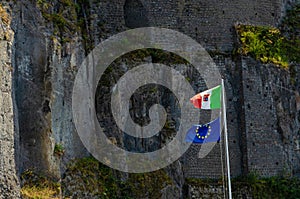 Italian and european union flags waving on an ancient brick wall background.