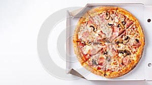 Italian fast food. Delicious hot pizza in a box with ham and champignons sliced and served on brown white table, close up view.