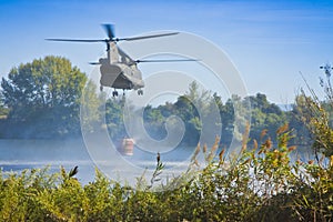 Italian fire fighting helicopter flying over a lake to collects water in a bucket to extinguish a fire