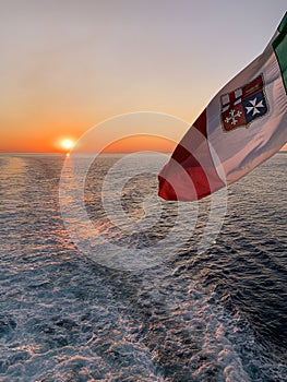 Italian flag waving on a ship sailing at dusk