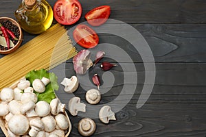 Italian food background, with tomatoes, parsley, spaghetti, mushrooms, oil, lemon, peppercorns on dark wooden table. Top view