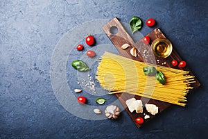 Italian food background with uncooked spaghetti, tomato, basil, cheese, garlic and olive oil for cooking pasta on dark stone table
