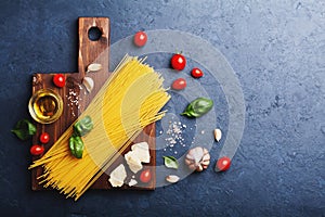 Italian food background with uncooked spaghetti, tomato, basil leaves, cheese, garlic and olive oil for cooking pasta.