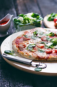 Italian food, cuisine. Margherita pizza on a black, wooden table with igredients like tomatoes, salad, cheese, mozzarella, basil.