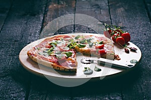 Italian food, cuisine. Margherita pizza on a black, wooden table with igredients like tomatoes, salad, cheese, mozzarella, basil.