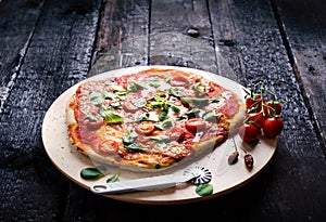 Italian food, cuisine. Margherita pizza on a black, wooden table with igredients like tomatoes, salad, cheese, mozzarella, basil.