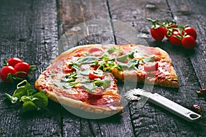 Italian food, cuisine. Margherita pizza on a black, wooden table with igredients like tomatoes, salad, cheese, mozzarella, basil.
