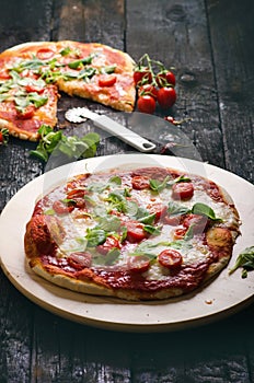 Italian food, cuisine. Margherita pizza on a black, wooden table with igredients like tomatoes, salad, cheese, mozzarella, basil.