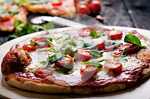 Italian food, cuisine. Margherita pizza on a black, wooden table with igredients like tomatoes, salad, cheese, mozzarella, basil.