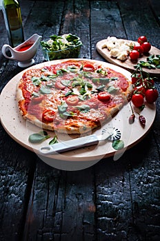 Italian food, cuisine. Margherita pizza on a black, wooden table with igredients like tomatoes, salad, cheese, mozzarella, basil.