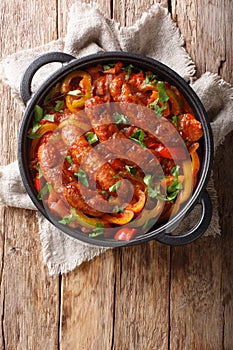 Italian food grilled sausage with grilled peppers, onions, herbs and tomatoes closeup in a frying pan. Vertical top view