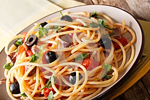 Italian food: spaghetti alla putanesca with anchovies, tomatoes, garlic, black olives and greens close-up. horizontal