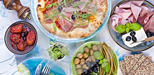 Italian food on the table, pizza and antipasto. Beautiful serving for a family dinner. Olives and basil. Cheese and ham