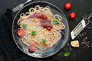 Italian food, traditional pasta spaghetti with tomato sauce, parmesan cheese and greens on a black stone background. View from