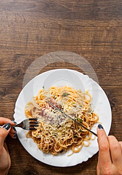 Italian food. woman hand holding fork with spaghetti bolognese in white plate on wooden table. with copy space