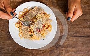 Italian food. woman hand holding fork with spaghetti bolognese in white plate on wooden table. with copy space