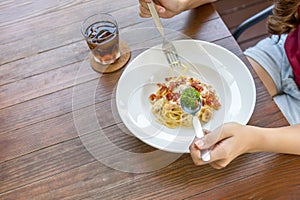 Italian food. woman hand holding fork and spoon with spaghetti carbonara in white plate on wooden table. top view. with copy space