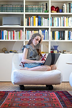 Girl sitting on an armchair writes on her computer