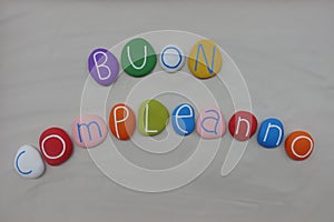 Buon Compleanno, italian Happy Birthday with colored stones over white sand photo